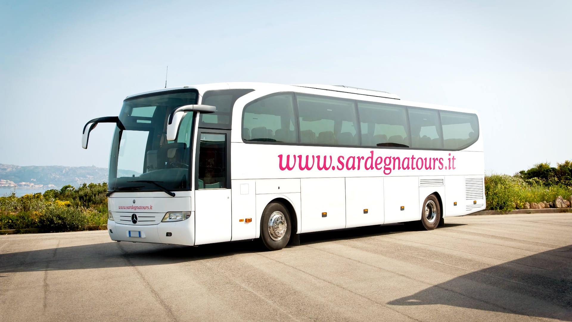 un pullman gran turismo bianco con la scritta Sardegnatours parcheggiato di fronte al mare